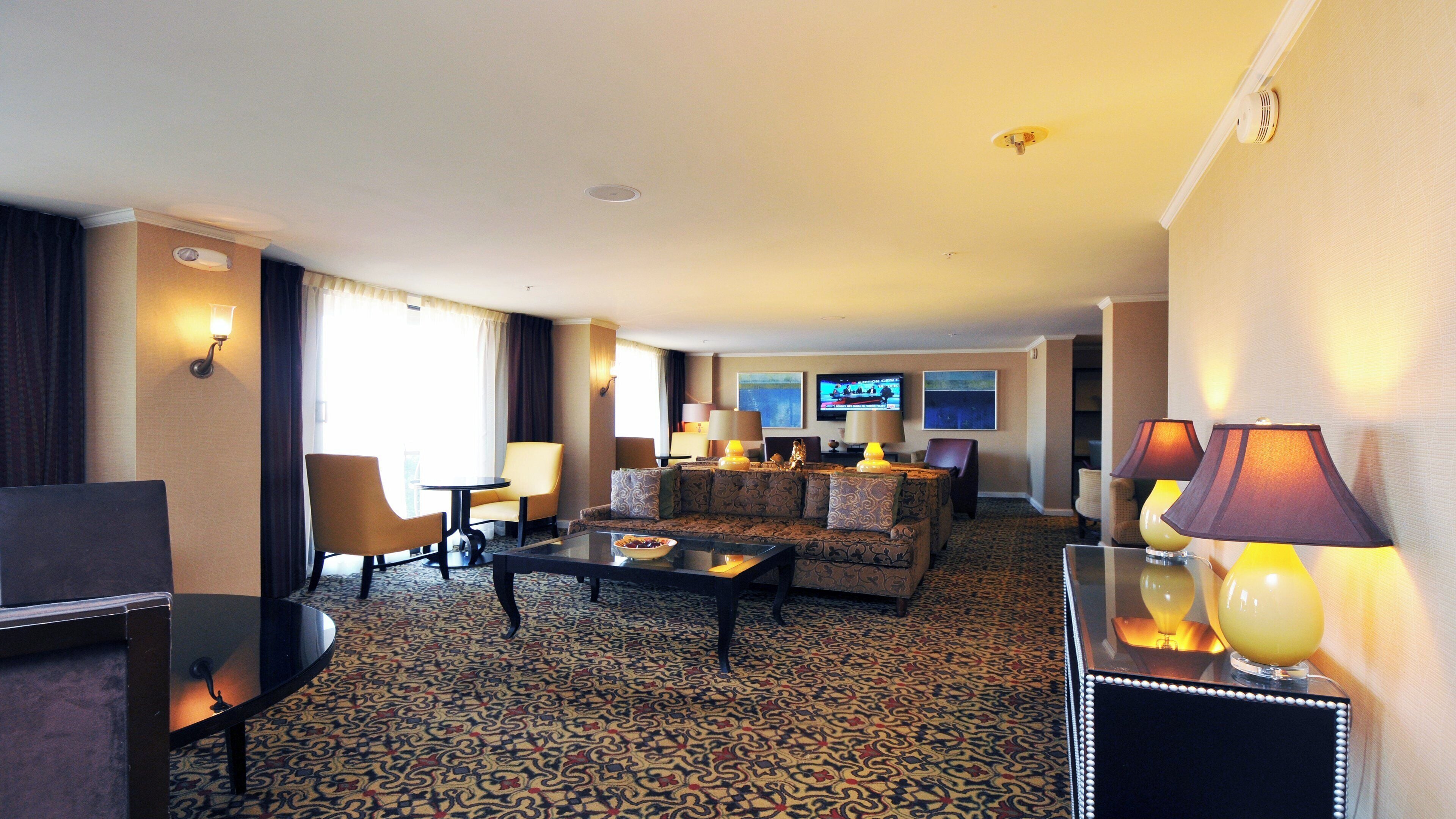 Habitación de hotel con alfombra estampada, un sofá, una mesa de centro, un televisor y dos lámparas.
