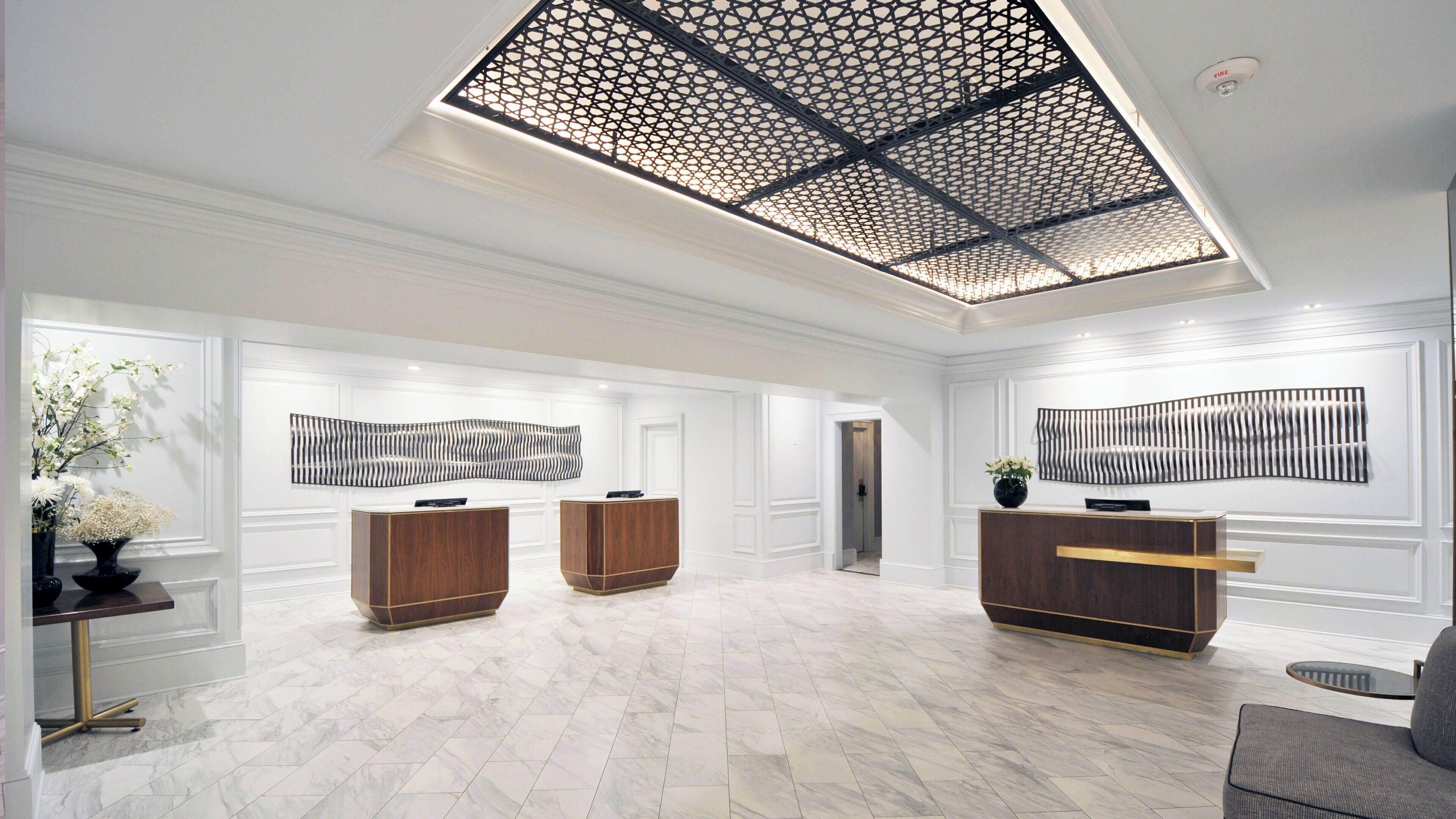 A spacious lobby with a high ceiling, two reception desks, and a modern abstract art piece on the wall.