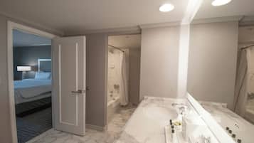 A hotel bathroom with a large bathtub, a separate shower area, and a bedroom visible through an open door.