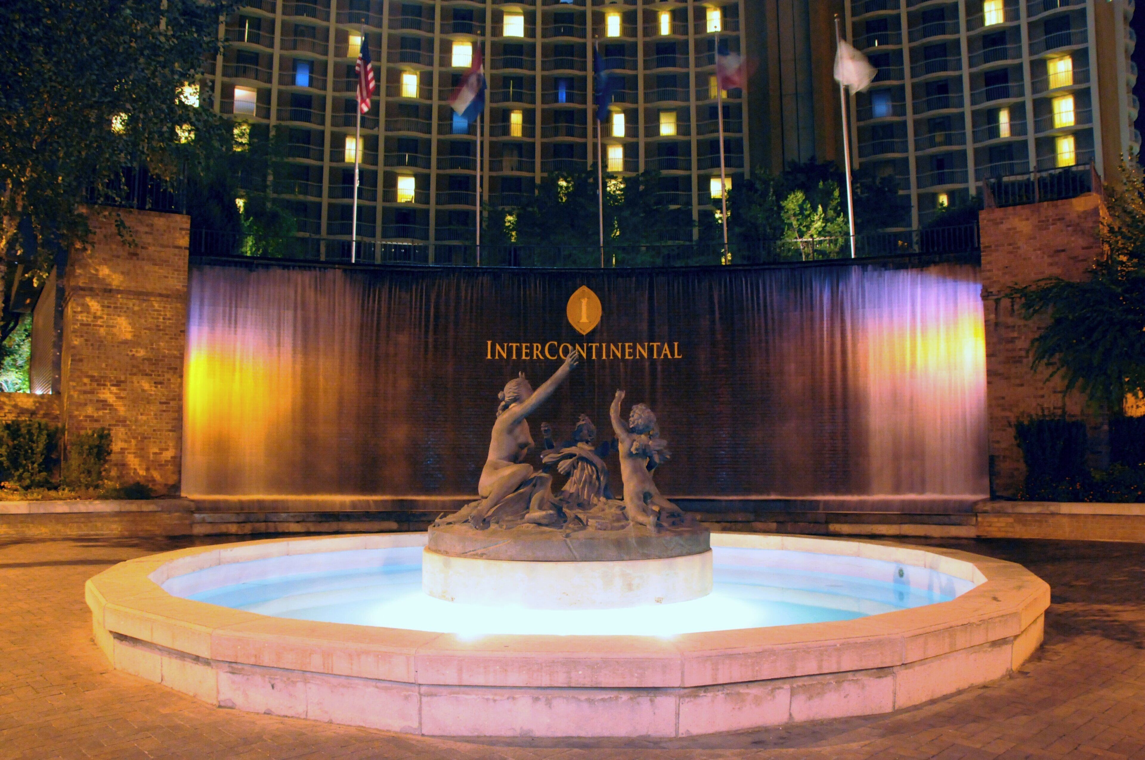Ein Brunnen mit einer Skulptur vor einem Gebäude mit beleuchteten Fenstern und einem Schild, auf dem 'INTERCONTINENTAL' steht.