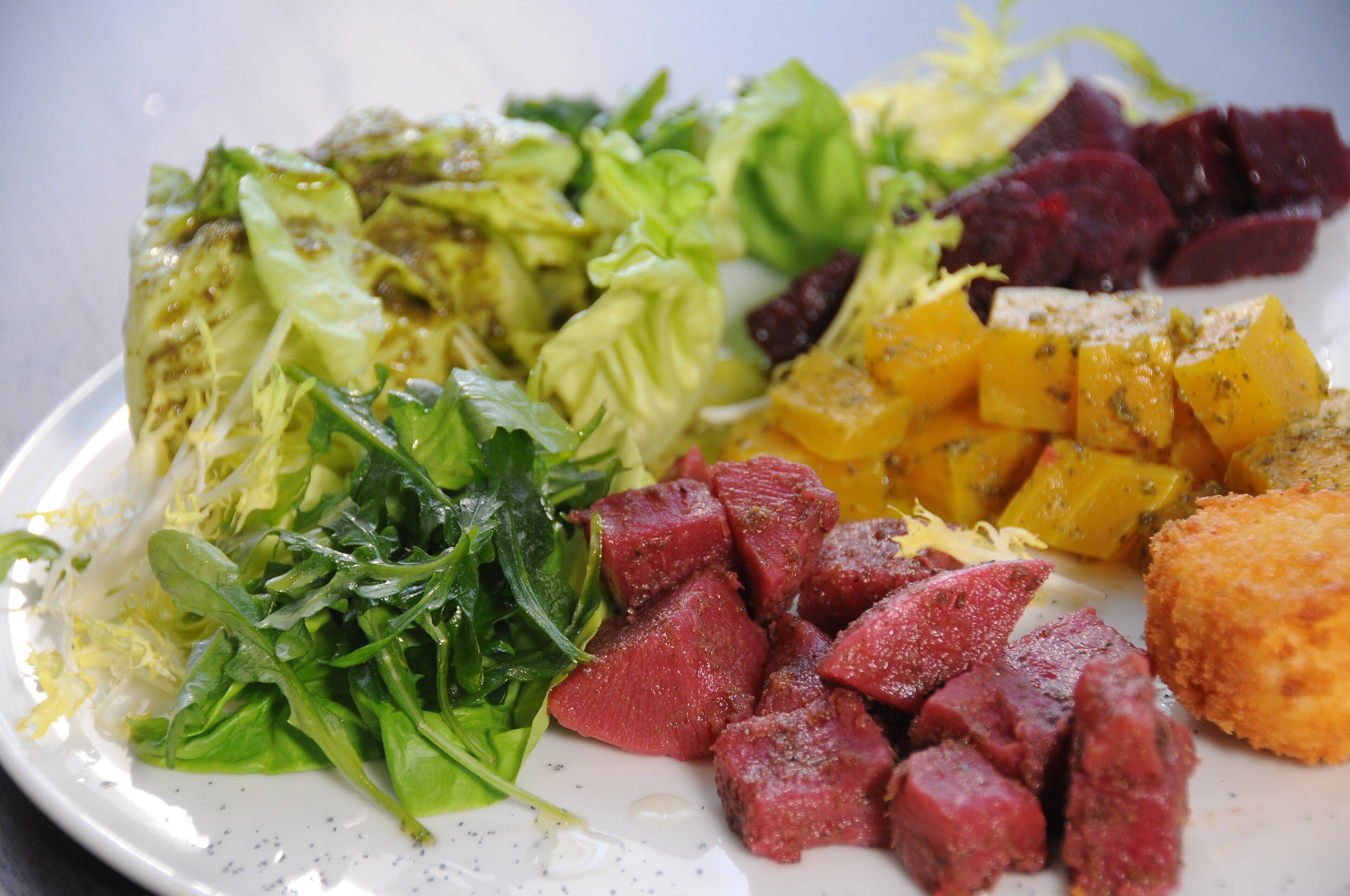 A plate with various food items including greens, beets, and cubed meat.
