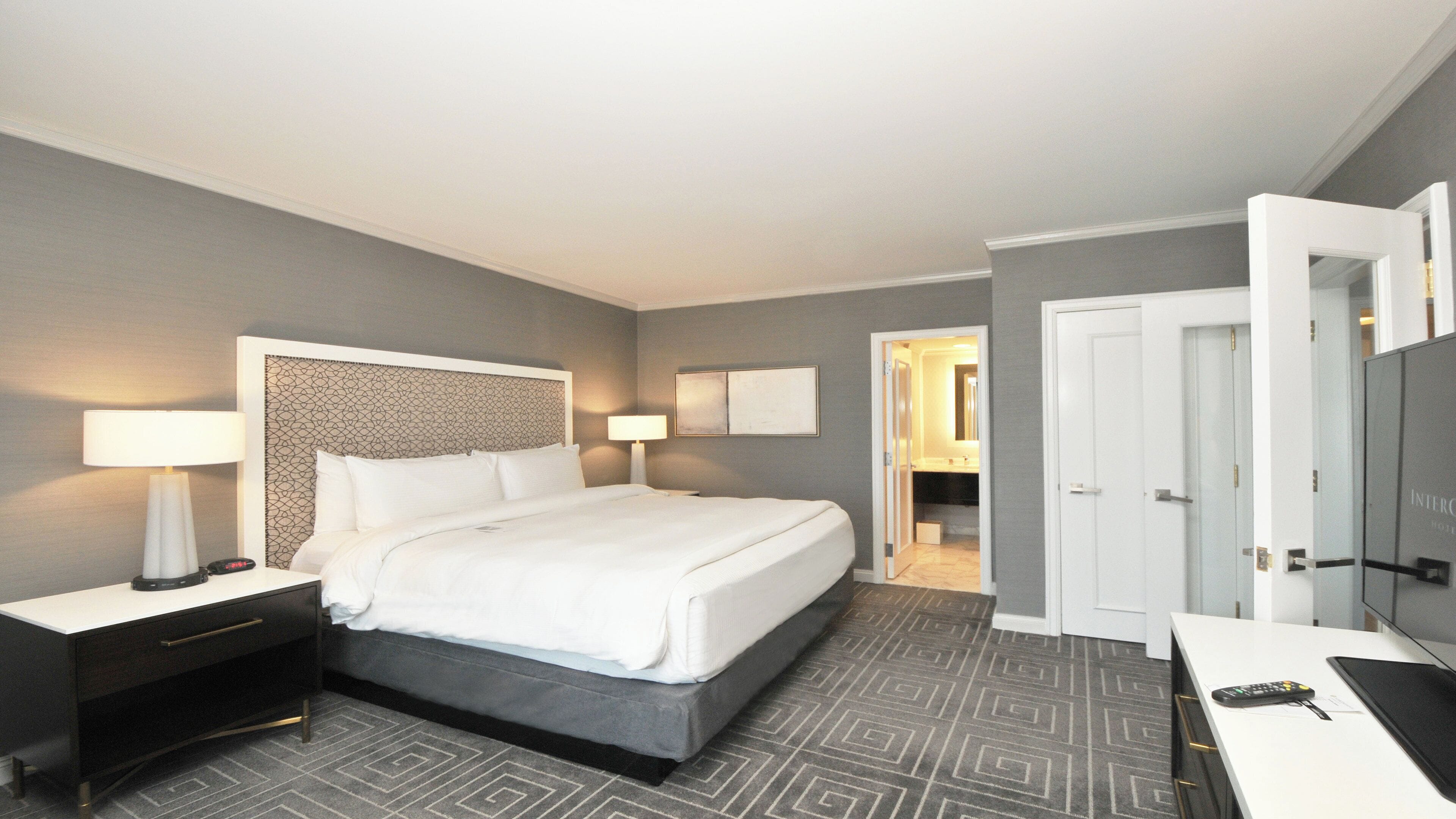 A hotel room with a bed, bedside tables, a desk, and a TV.