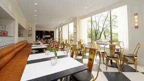 Un restaurant avec un sol à carreaux, des tables blanches et noires, et des chaises dorées. Les murs sont ornés de tableaux encadrés, et un banc est placé le long du mur.
