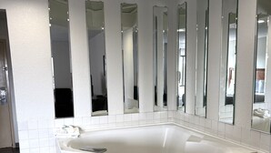 Ein modernes Badezimmer mit einer großen Badewanne, mehreren Spiegeln und Einbaustrahler.
