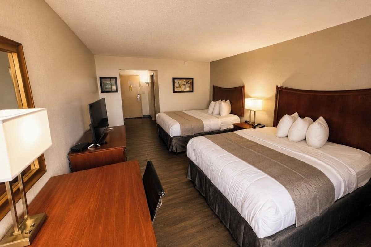 A hotel room with two beds, a desk, a chair, a TV, and a lamp.