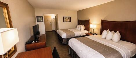 A hotel room with two beds, a desk, a chair, a TV, and a lamp.