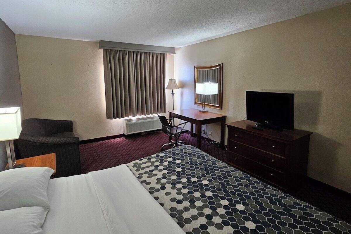 A hotel room with a bed, a desk with a chair, a television, a lamp, and a window with curtains.
