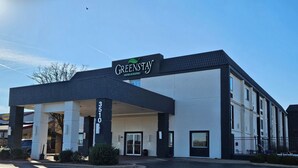 Ein GreenStay Hotel mit modernem Design, das eine überdachte Einfahrt, ein gut sichtbares Adressenschild und einen klaren Himmel im Hintergrund zeigt.
