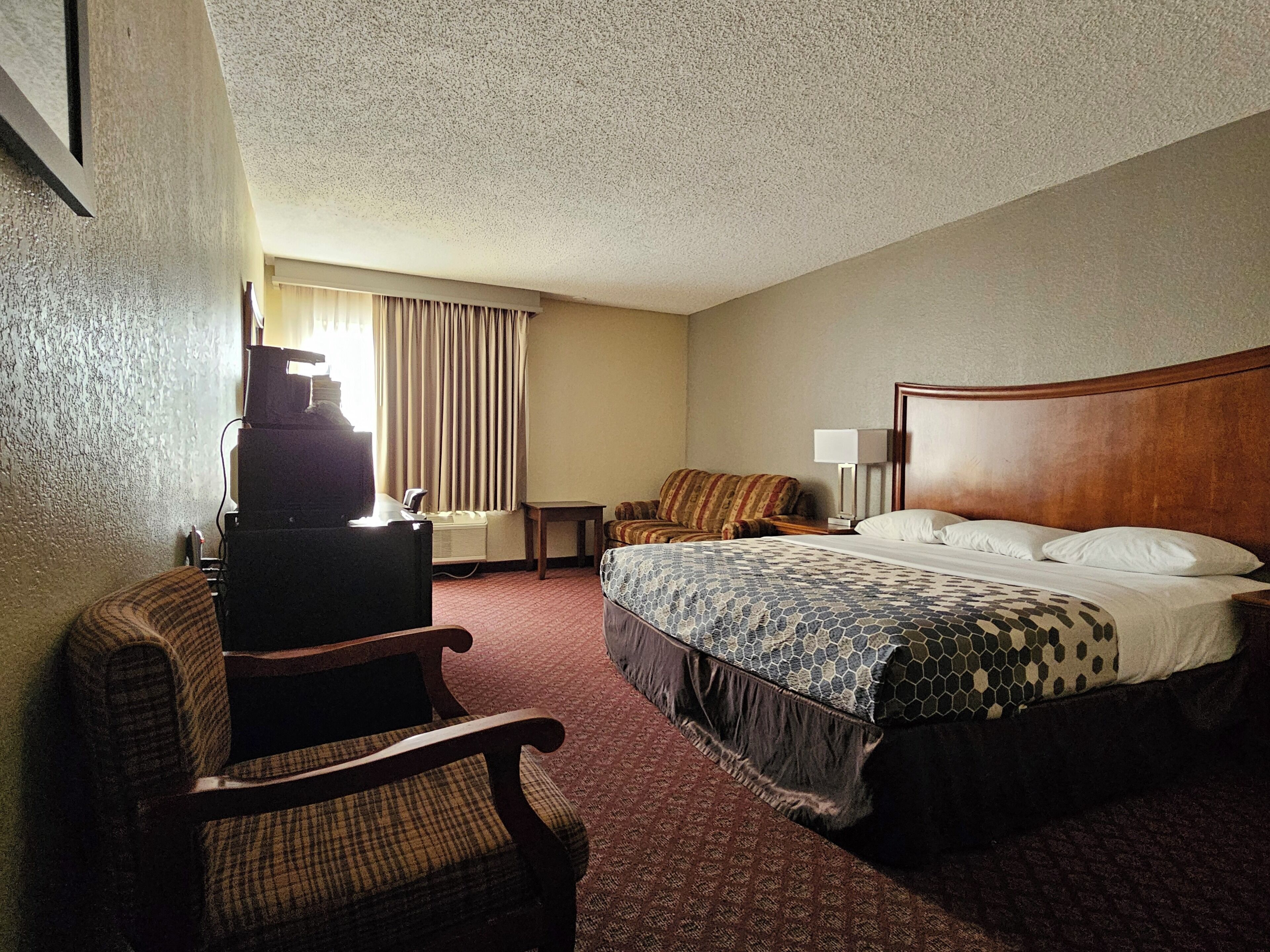 A hotel room with a bed, a desk, a chair, a lamp, and a window with curtains.