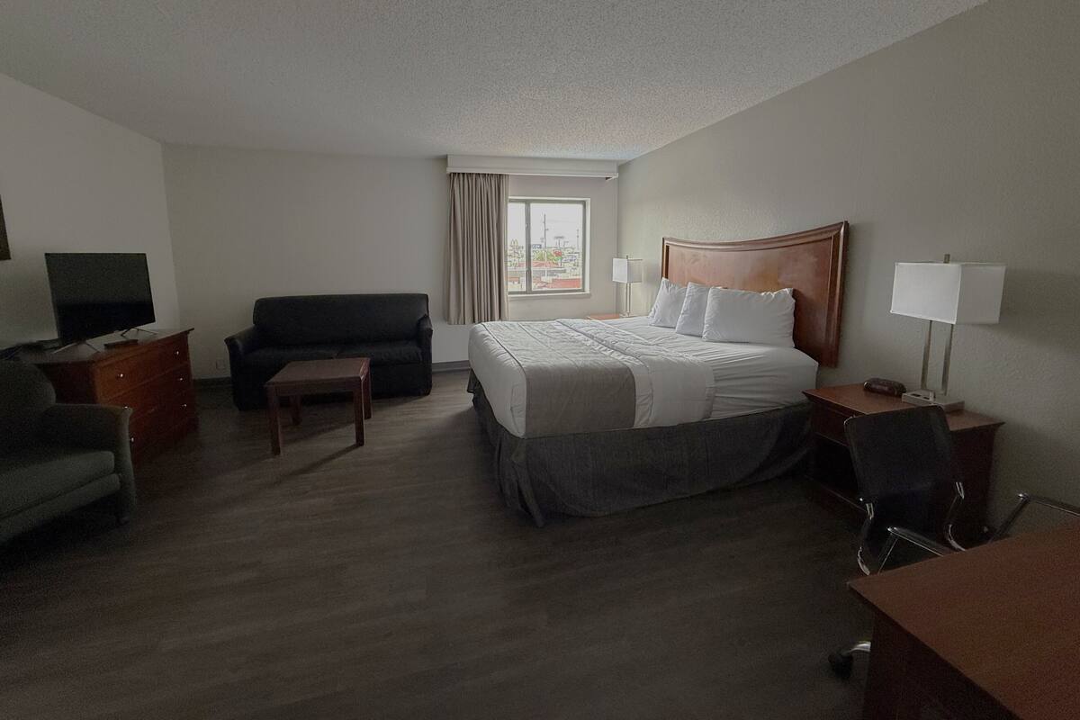 A hotel room with a bed, a sofa, a desk, a chair, a TV, and a window with curtains.