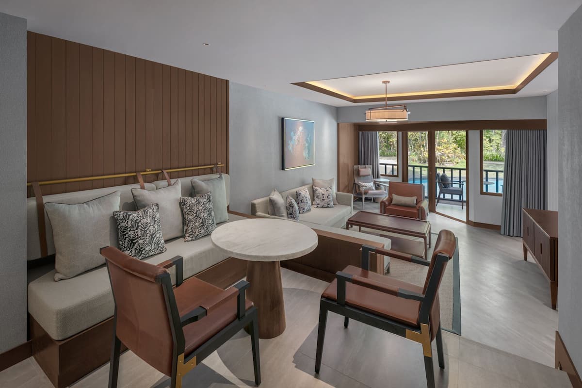 A modern living room with a sofa set, coffee table, and chairs. There is a dining area with a table and chairs. The room has large windows and a view of a pool.