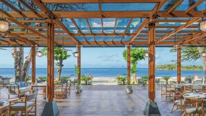 An outdoor seating area with wooden tables and chairs, potted plants, and a view of the beach and ocean. - The Laguna, a Luxury Collection Resort & Spa, Nusa Dua, Bali (Nusa Dua)