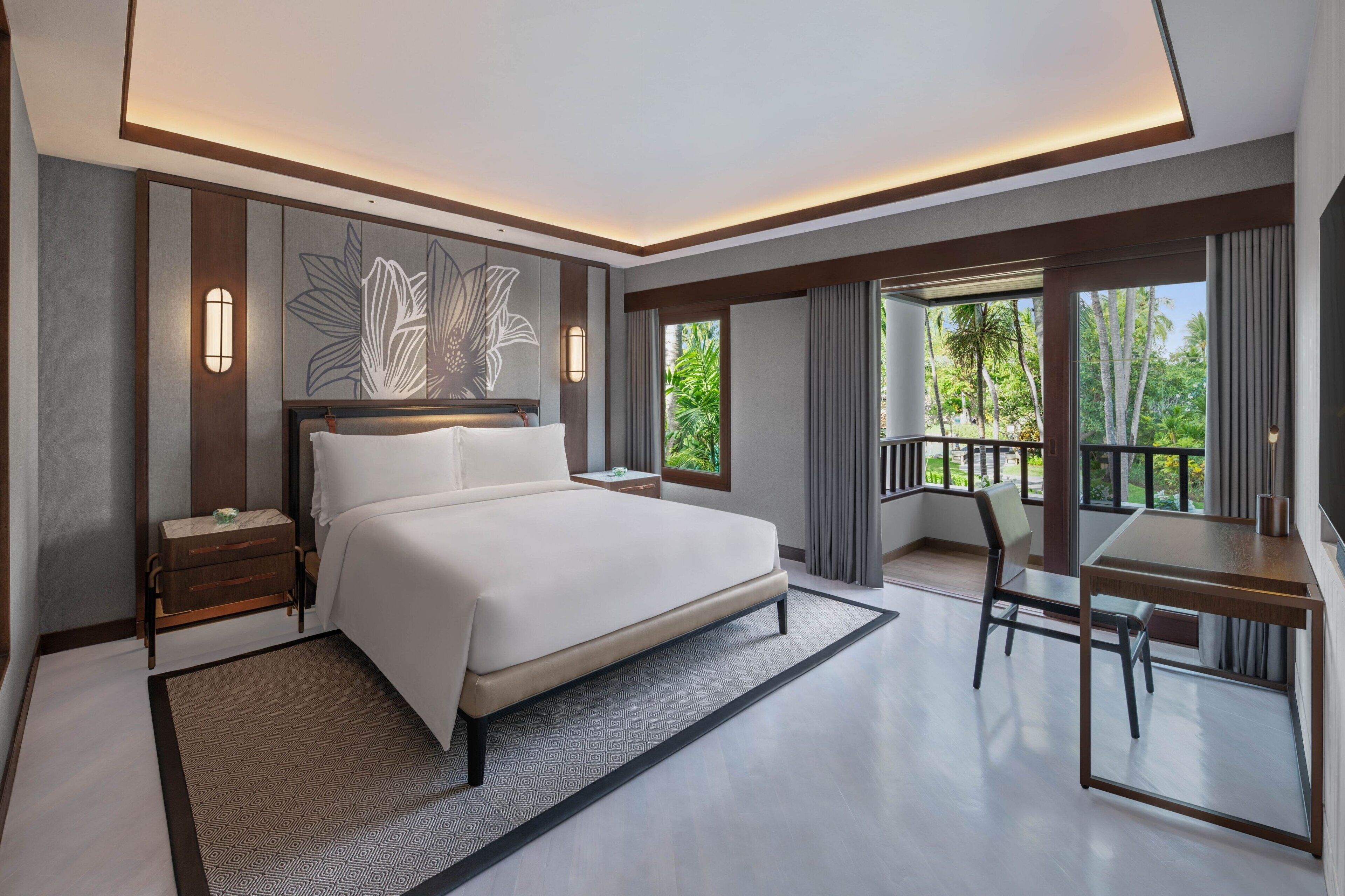 Ein modernes Hotelzimmer mit einem großen Bett, einem Schreibtisch und einem Balkon mit Blick auf Grünflächen.