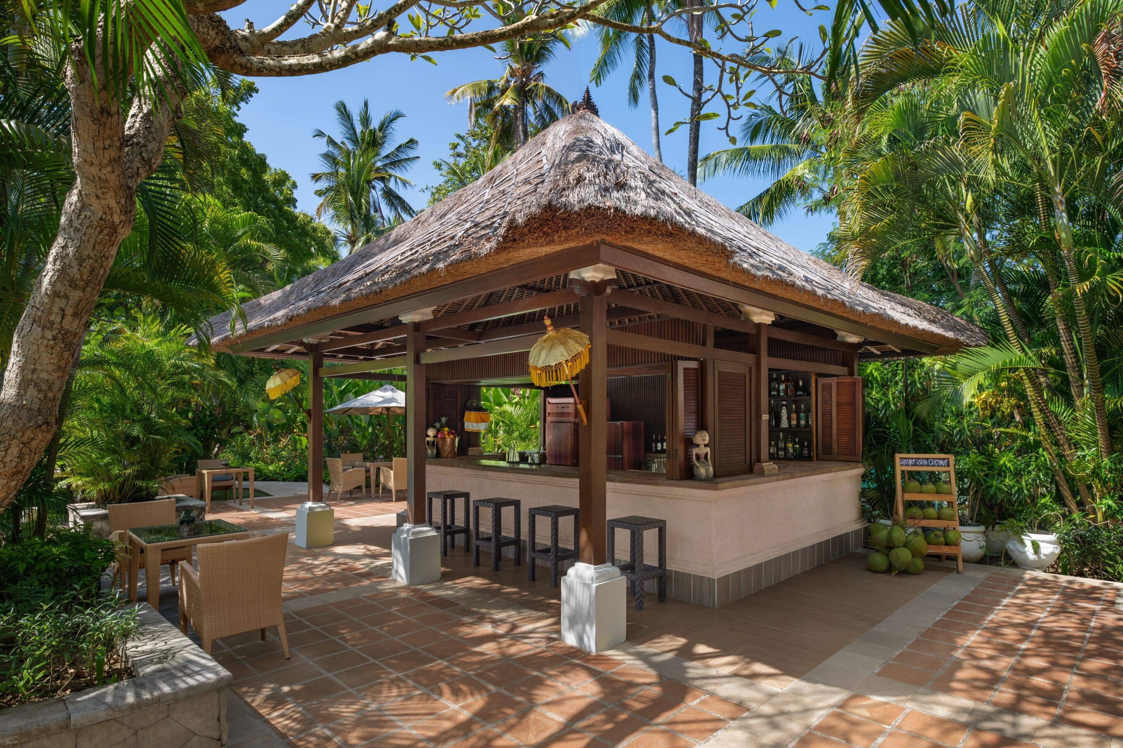 A thatched-roof bar area with outdoor seating, surrounded by lush greenery and palm trees.