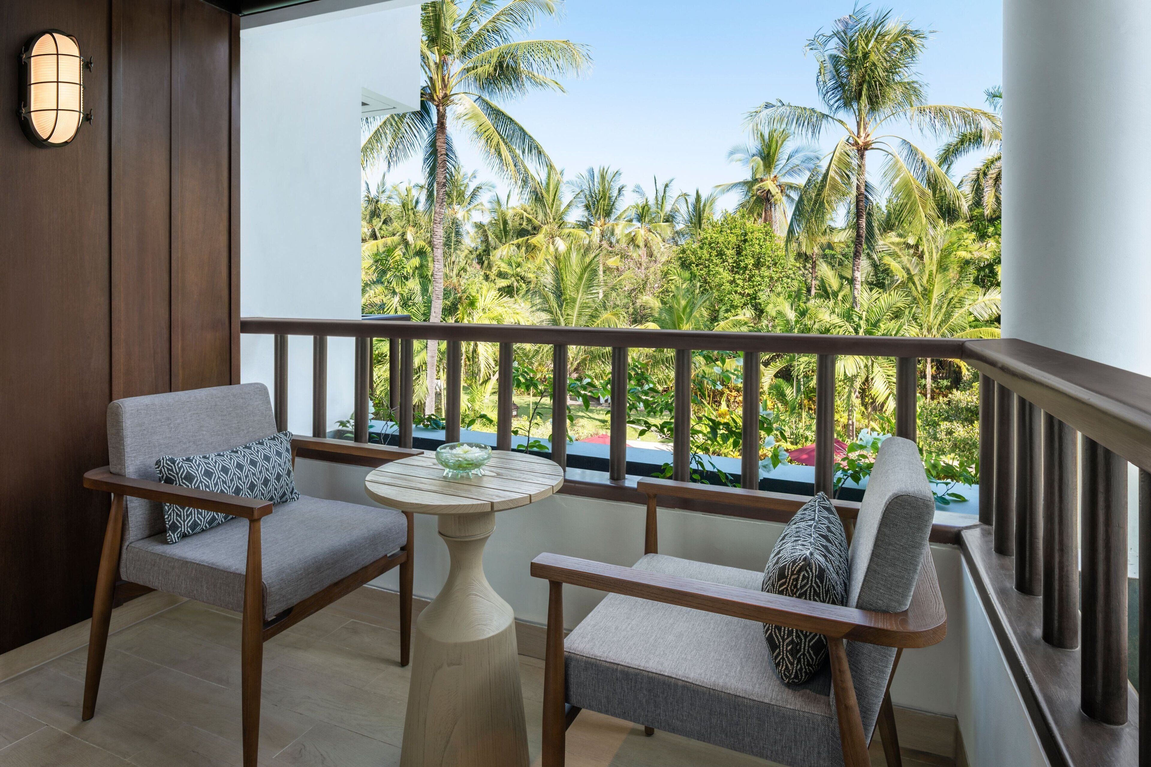Un balcon avec deux chaises et une petite table, donnant sur un jardin tropical agrémenté de palmiers.