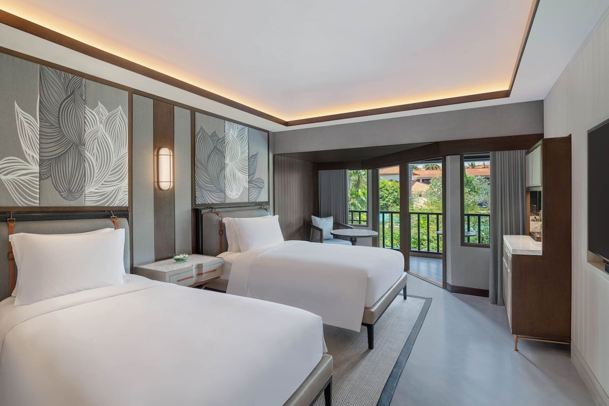 A modern hotel room with two beds, a TV, and a balcony with a view.