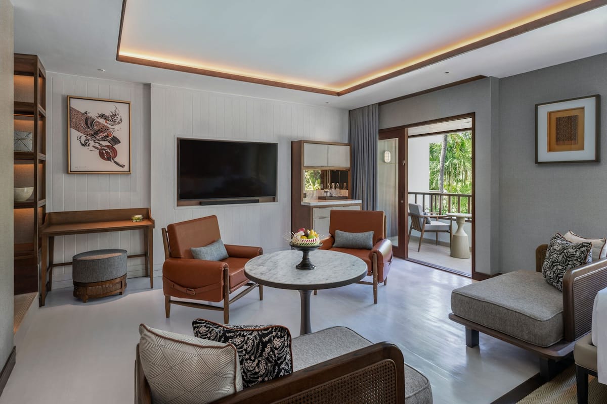 A modern living room with a flat-screen TV, comfortable seating, a round table with a centerpiece, and a balcony with a view.