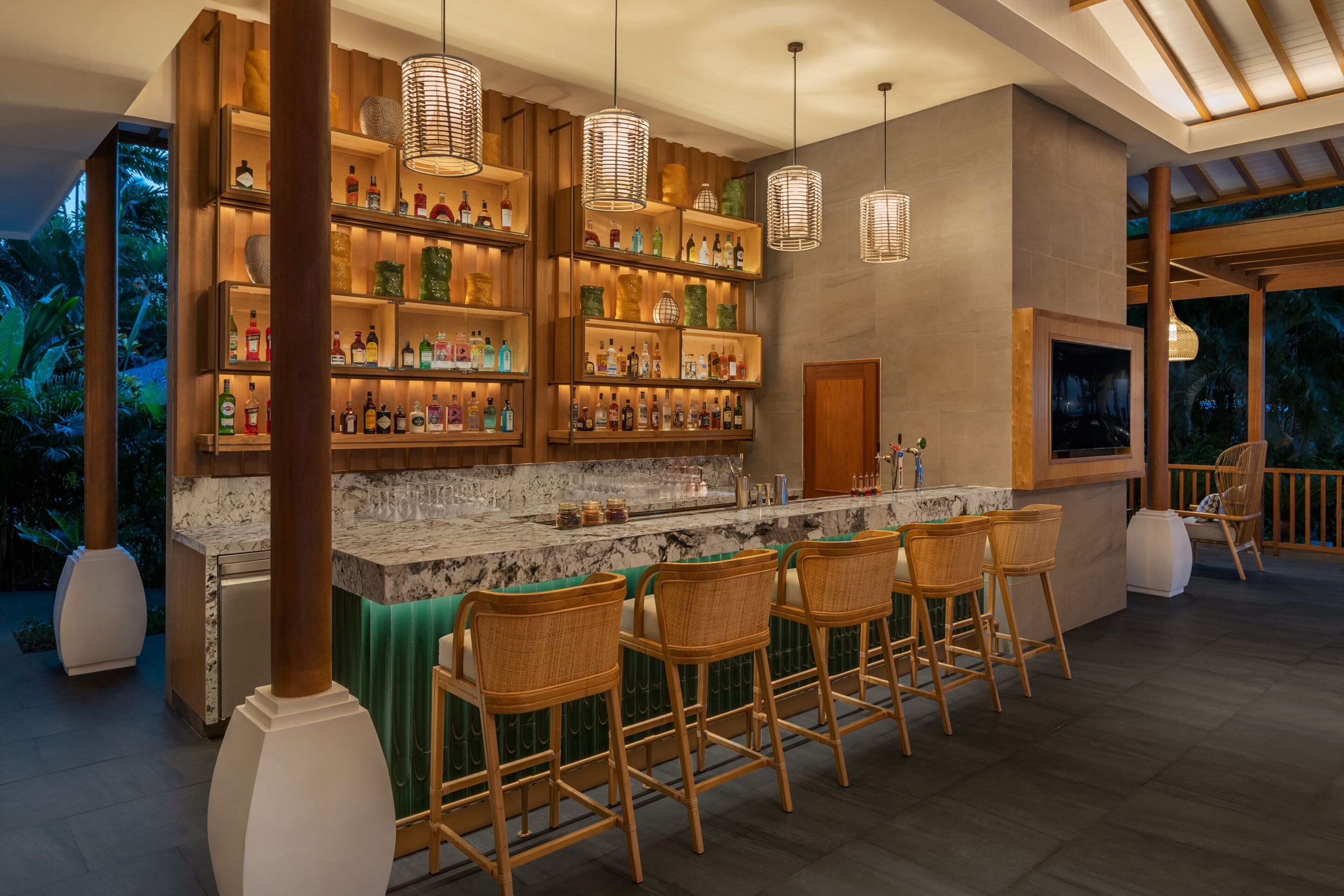 A bar area with wooden shelves, wicker chairs, and hanging lights.
