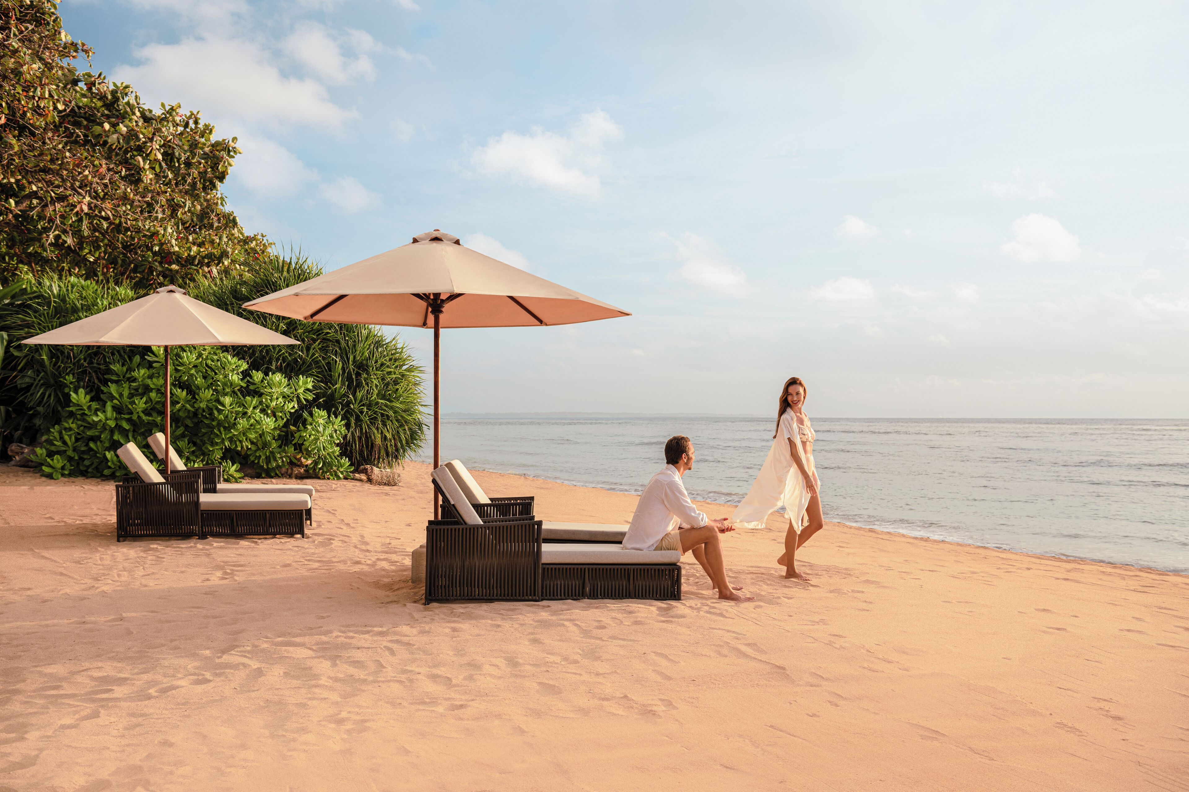 A beach setting with lounge chairs and umbrellas, a couple walking, and a view of the sea.