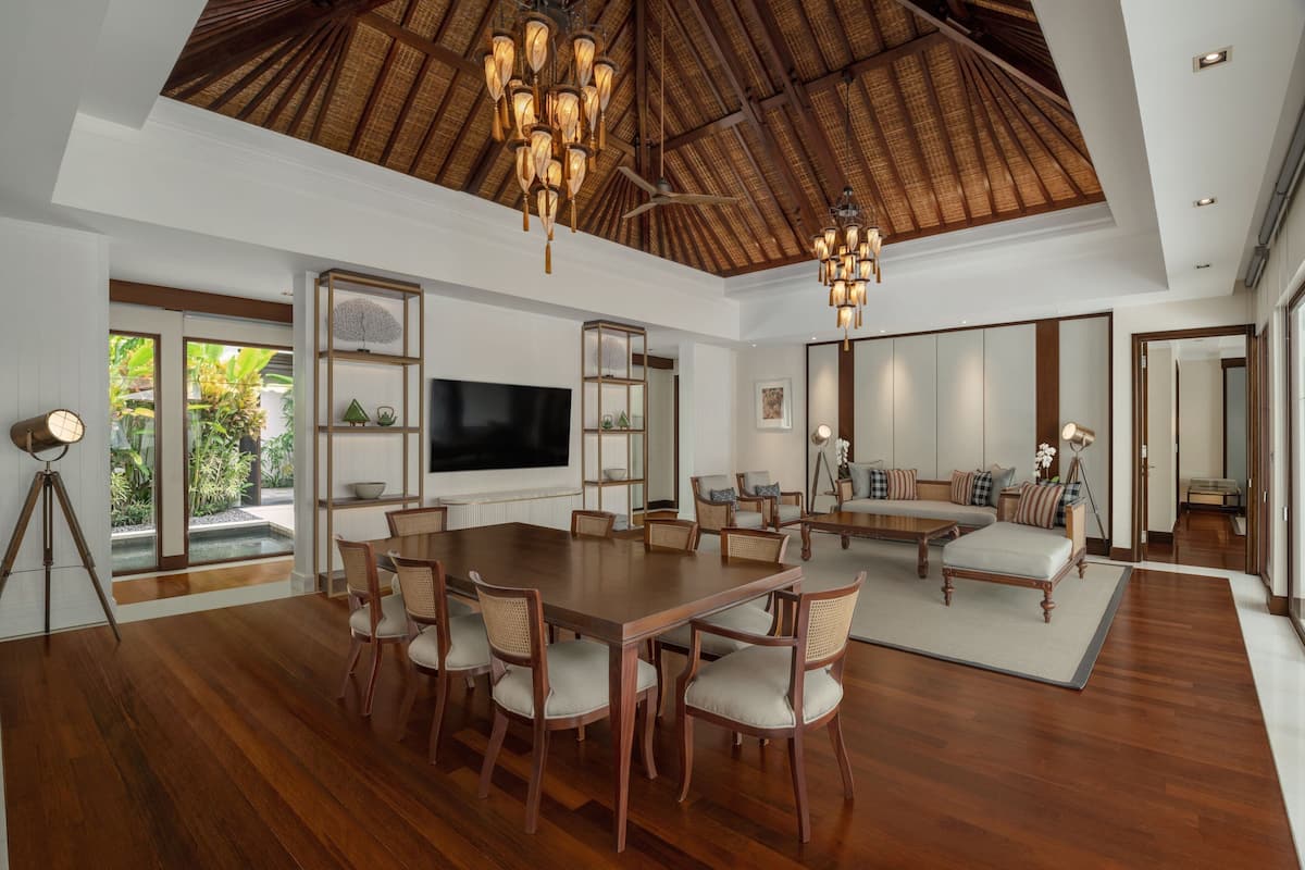 A spacious living area with a large wooden dining table, comfortable seating, a flat-screen TV, and a ceiling with a thatched design.