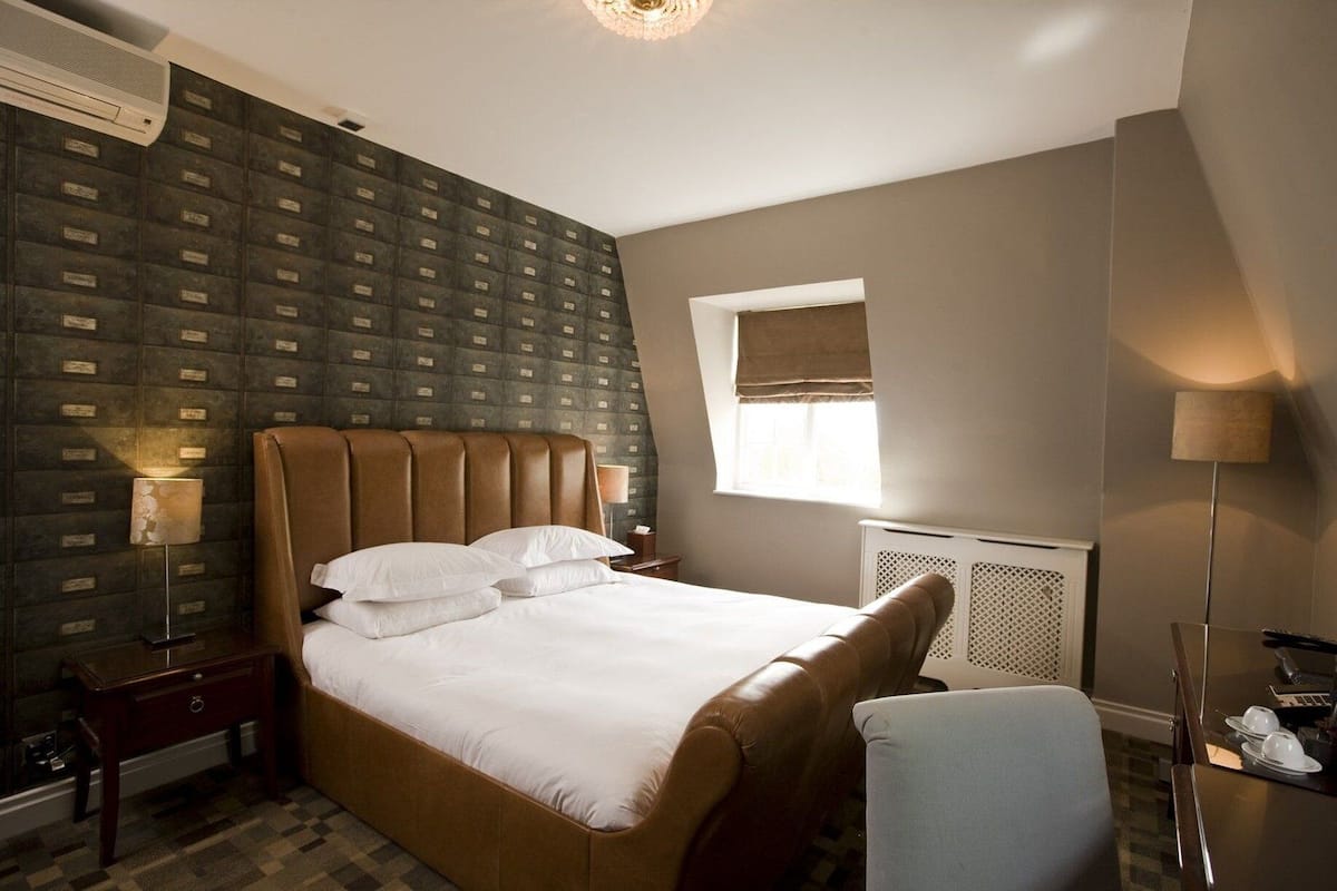 Hotelkamer met een groot bed, een raam met uitzicht, een radiator en een bureau met een lamp.