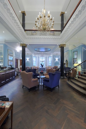 Eine großzügige Lobby mit einem prächtigen Kronleuchter, bequemen Sitzgelegenheiten, einer Bar und einer Treppe zu einer oberen Etage.