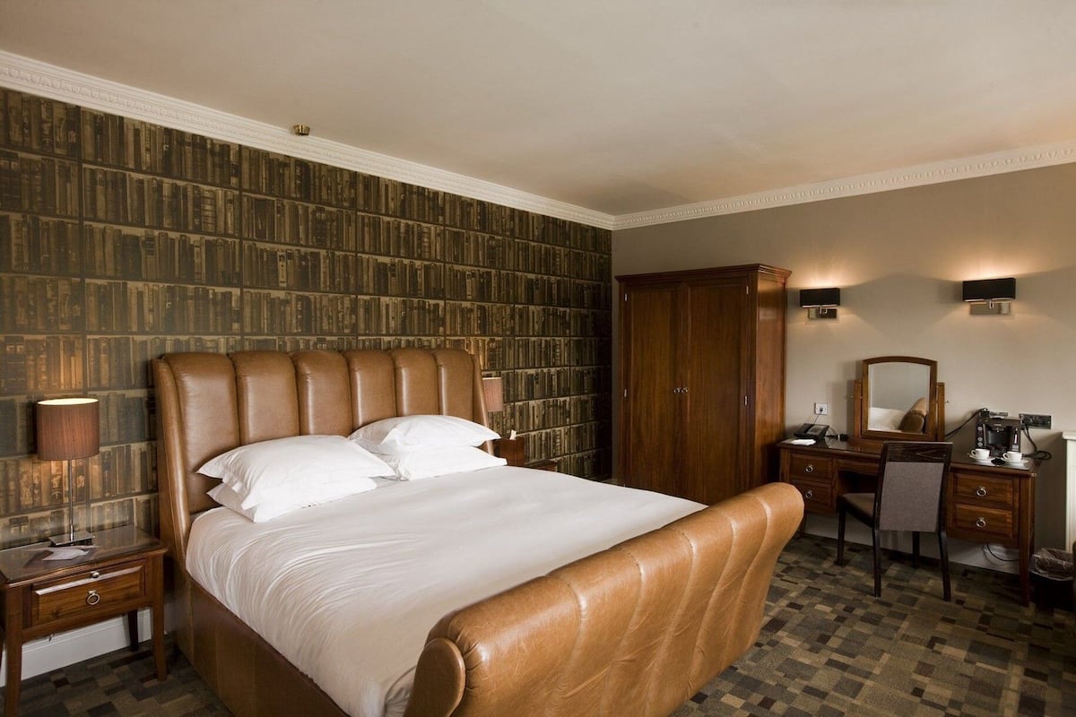 Een hotelkamer met een groot bed, een houten garderobe, een bureau met stoel, een bureaulamp en een boekenplank.