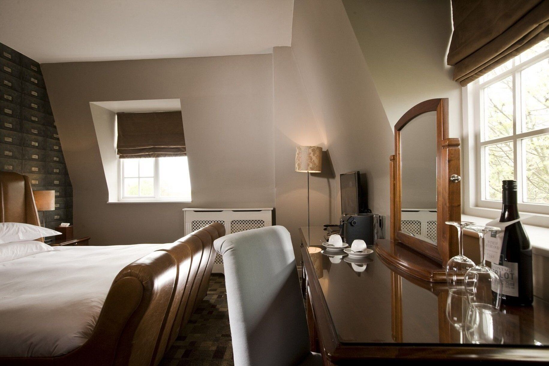 Een hotelkamer met een bed, een bureau met spiegel, een lamp en een raam met gordijnen.