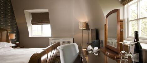 A hotel room with a bed, a desk with a mirror, a lamp, and a window with curtains.