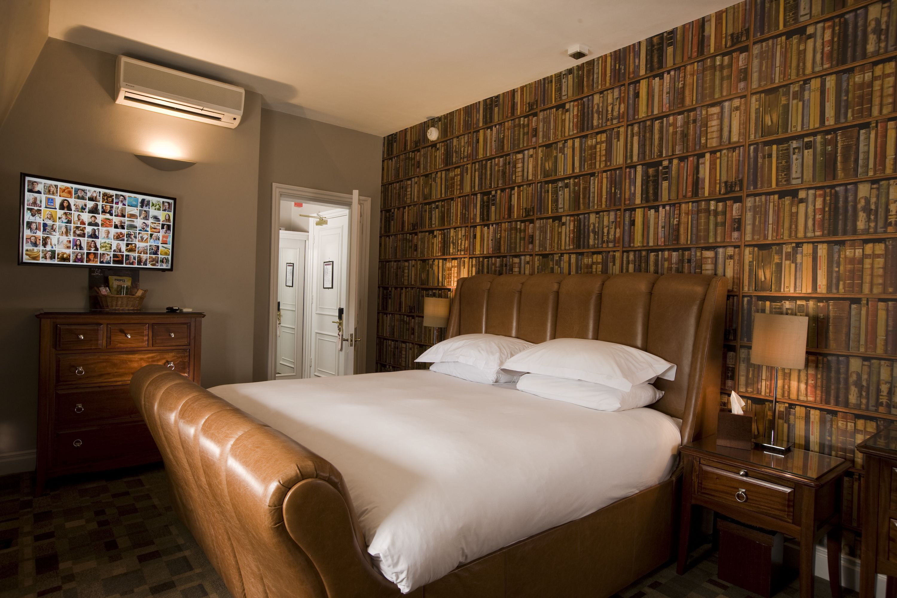 Une chambre d’hôtel avec un grand lit, une tête de lit en bois, une bibliothèque, une commode et un climatiseur fixé au mur.