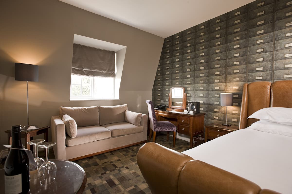 Hotelkamer met een bed, een bank, een bureau met stoel, een lamp en een raam met uitzicht.
