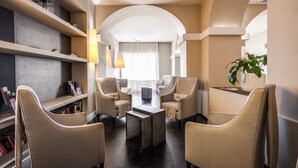 A modern hotel lobby with a central coffee table, comfortable seating, and a bookshelf. - Hotel Villafranca (Rome)