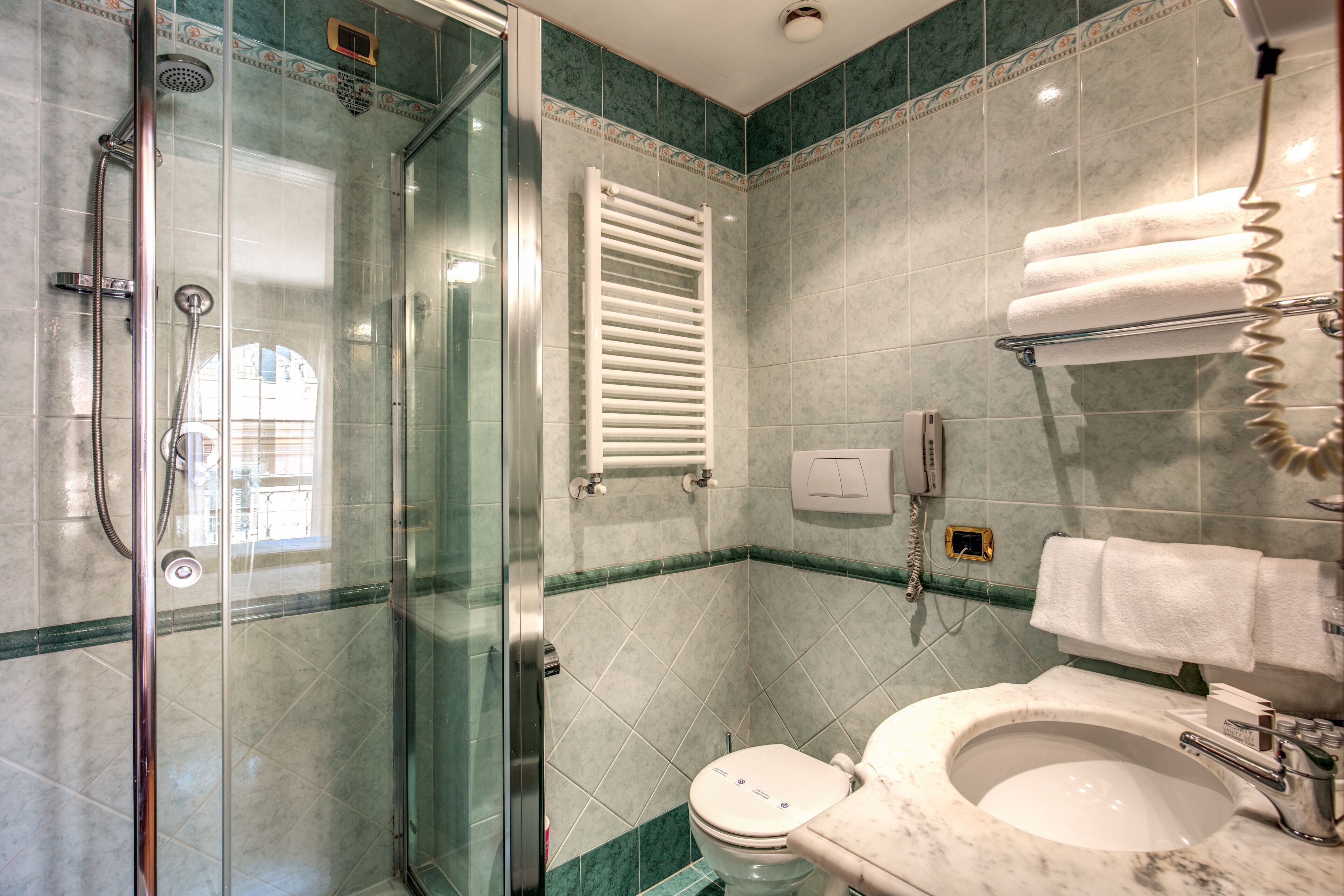 A bathroom with a glass-enclosed shower, a toilet, and a sink with a towel rack.