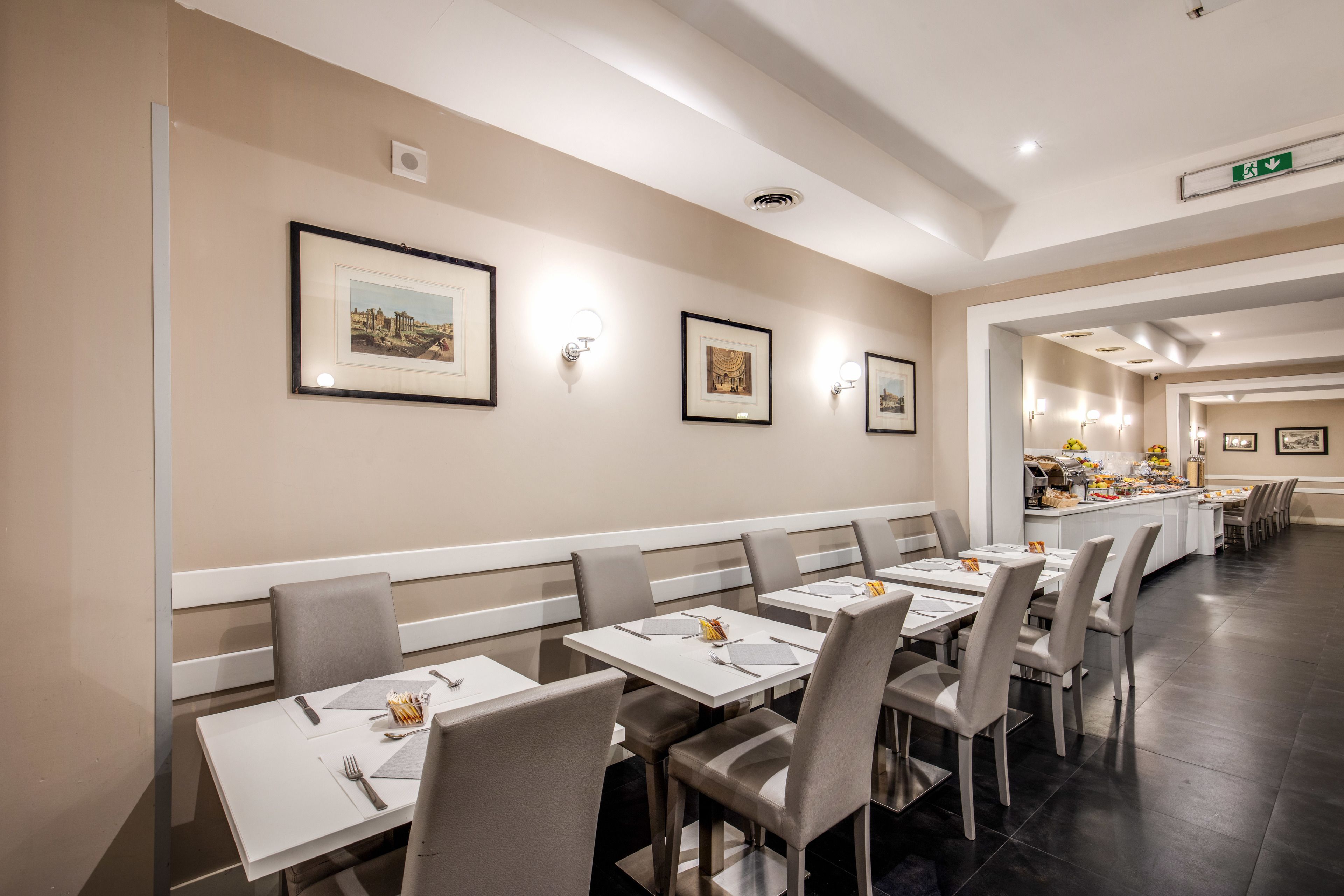 Ein Restaurant mit weißen Tischen und Stühlen, gerahmten Bildern an der Wand und einem Buffet im Hintergrund.