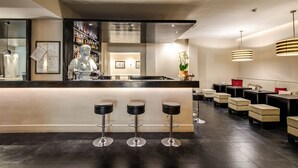 A modern bar area with a counter, stools, and tables. - Hotel Villafranca (Rome)