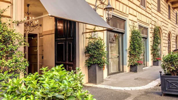 A building facade with a large awning, a chandelier, and potted plants. - Hotel Villafranca (Rome)