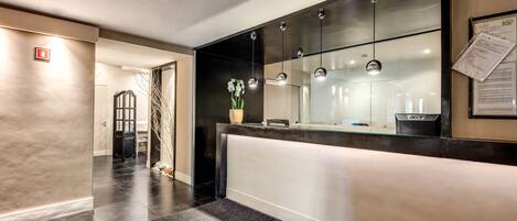 A modern reception area with a glass partition, a reception desk, and a wall-mounted information board.