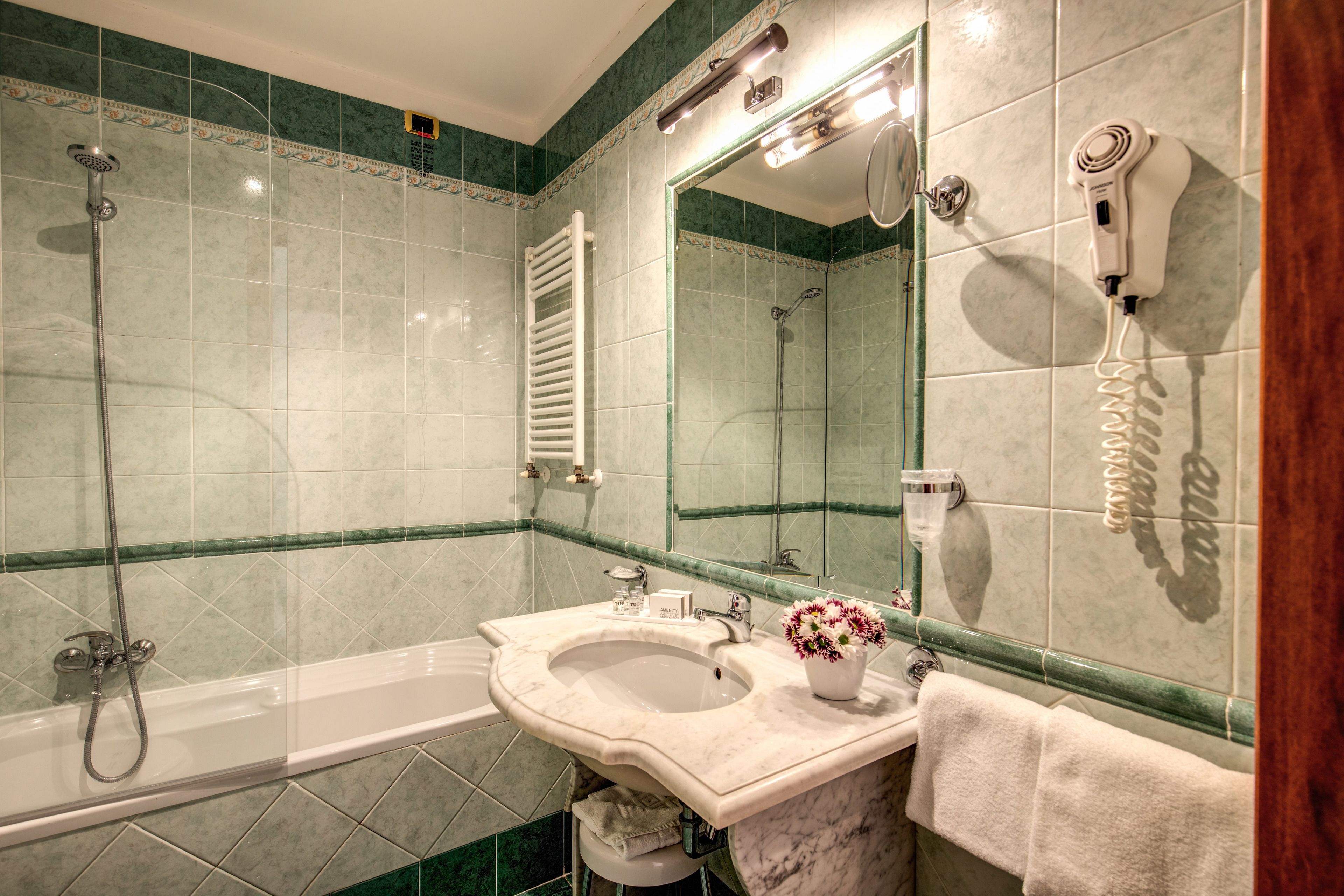 A bathroom with a bathtub, a sink, a mirror, and a hairdryer mounted on the wall.