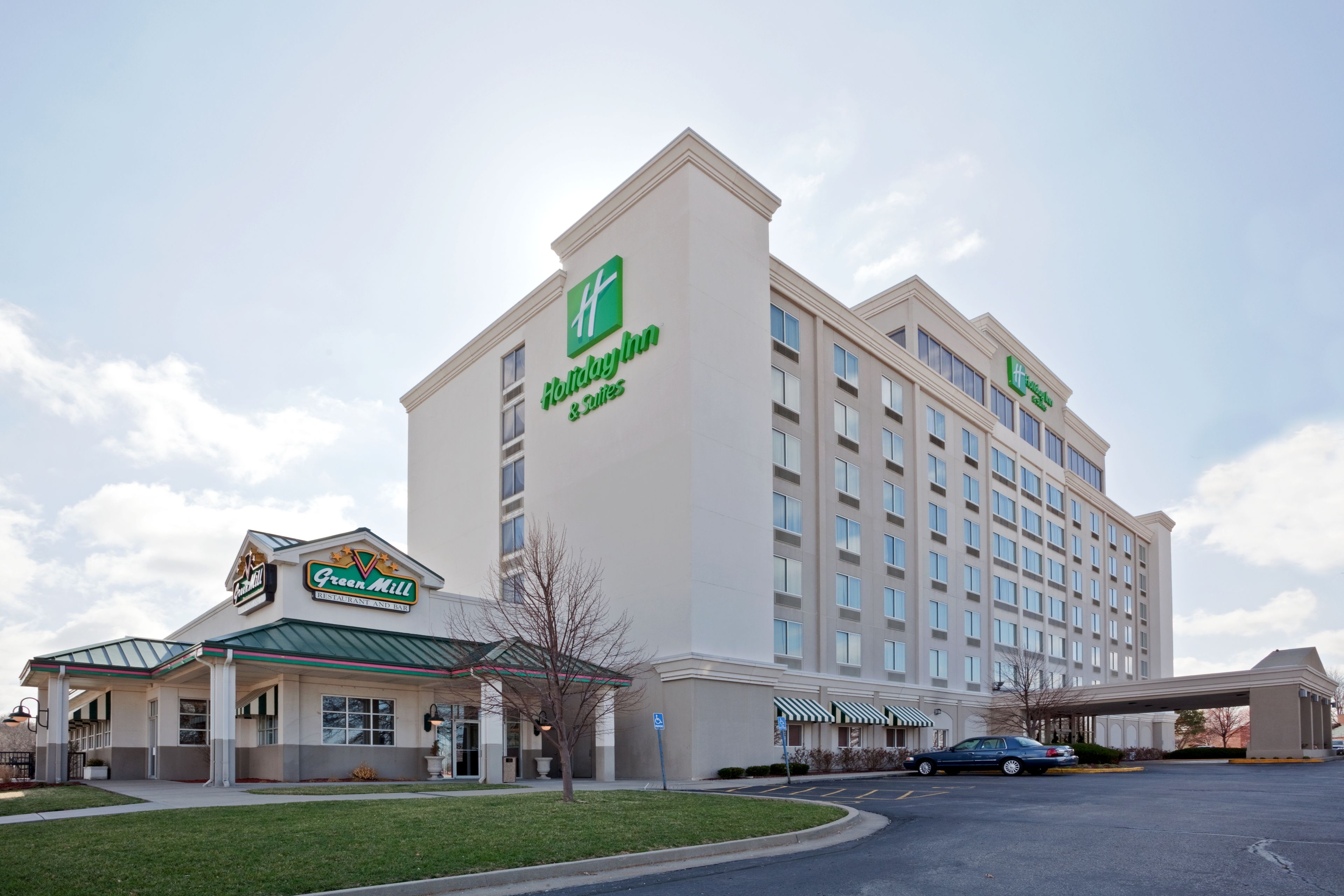 Un hotel Holiday Inn Express con fachada verde y blanca, un área exterior cubierta y un estacionamiento.