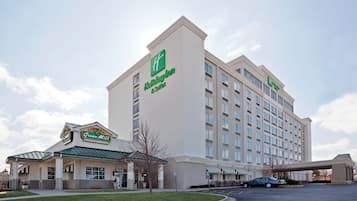 Un hotel Holiday Inn Express con fachada verde y blanca, un área exterior cubierta y un estacionamiento.