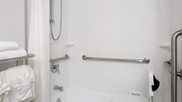Une salle de bain équipée d’une douche, de barres d’appui, de toilettes avec un siège de sécurité et de serviettes rangées sur un porte-serviettes.