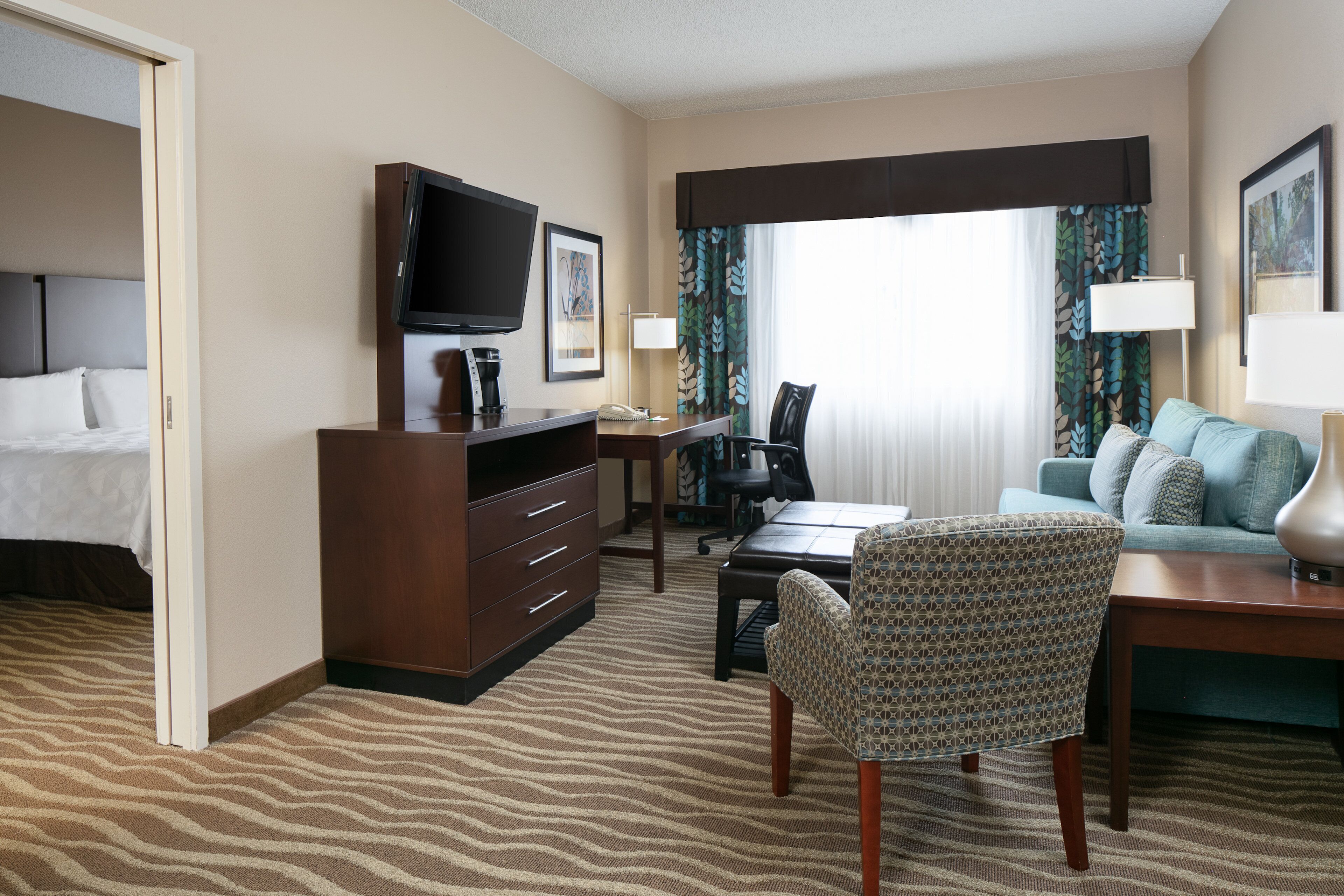 A hotel room with a bed, a desk, a chair, a television, and a window with curtains.