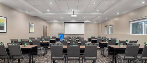 A conference room with a large screen, multiple tables, and chairs.