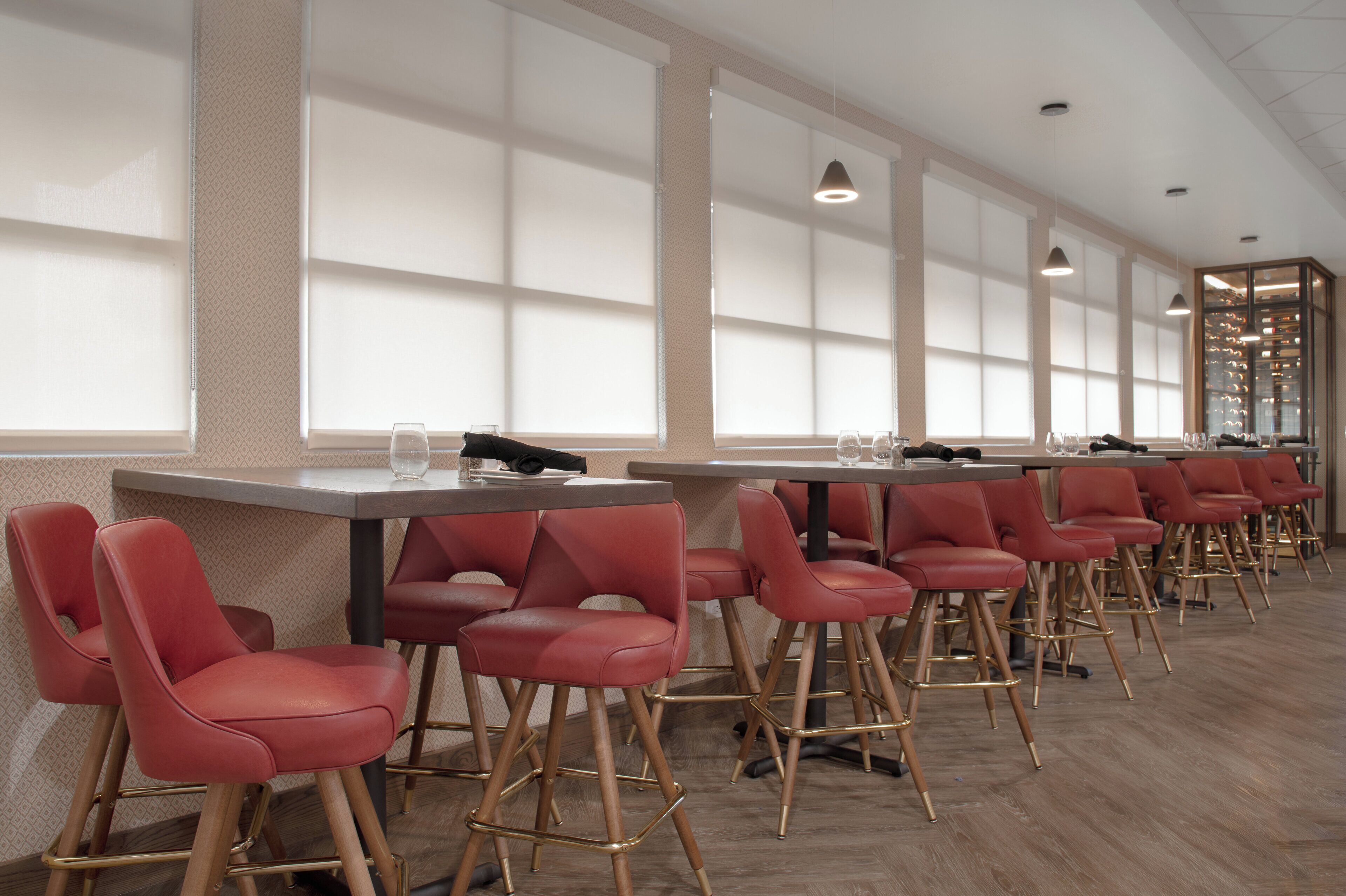 Una fila de taburetes rojos con patas de madera y una mesa con un vaso de agua y una servilleta.