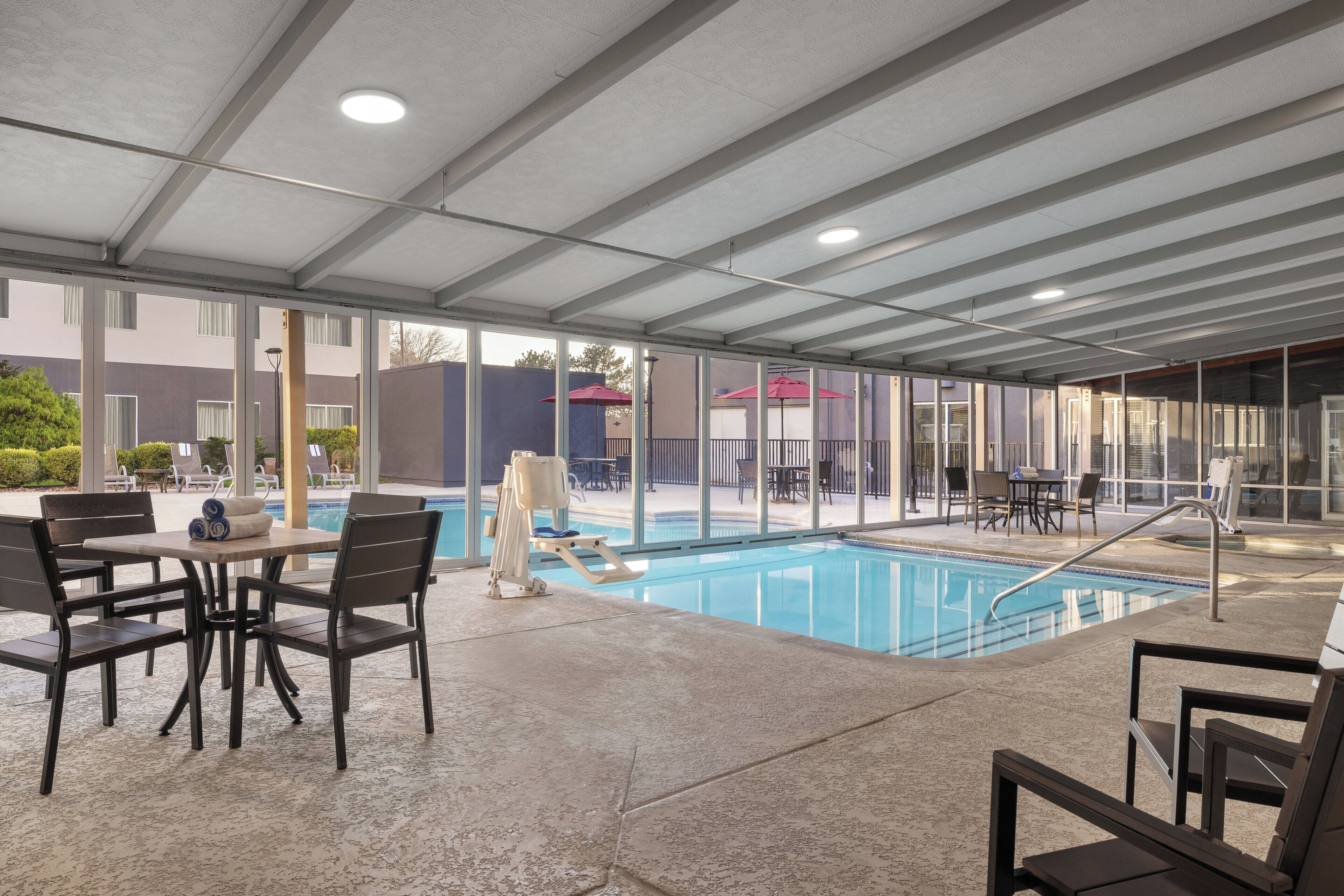 An indoor swimming pool with a covered area, seating arrangements, and a view of the outside.