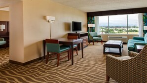 Habitación de hotel con escritorio, televisor, dos sillas, sof á y ventana grande con vistas a la ciudad.