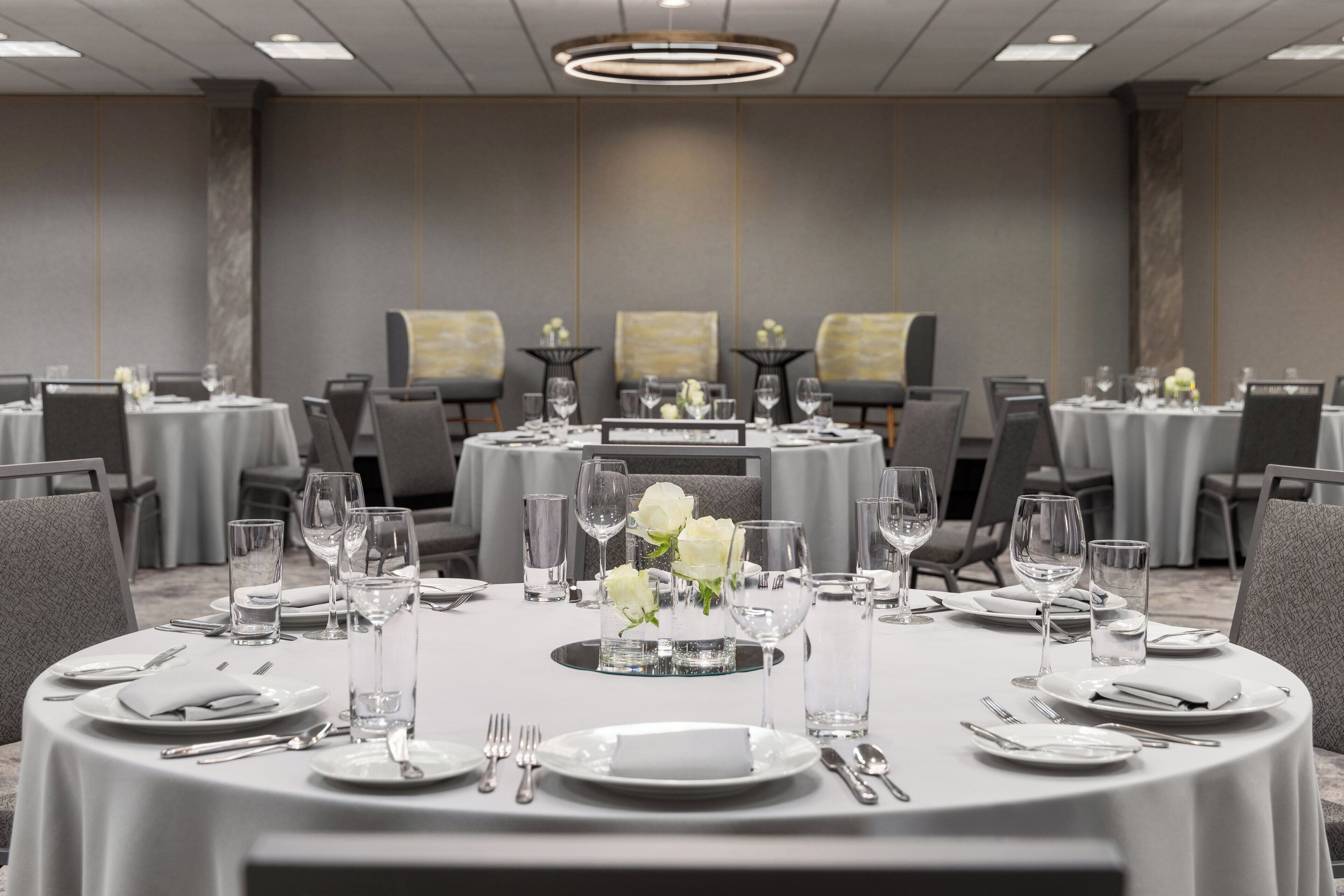 Un salón de conferencias con mesas redondas dispuestas para comedor, equipado con platos, cubiertos y vasos.