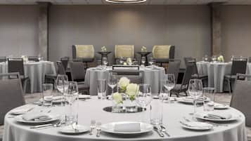 Un salón de conferencias con mesas redondas dispuestas para comedor, equipado con platos, cubiertos y vasos.