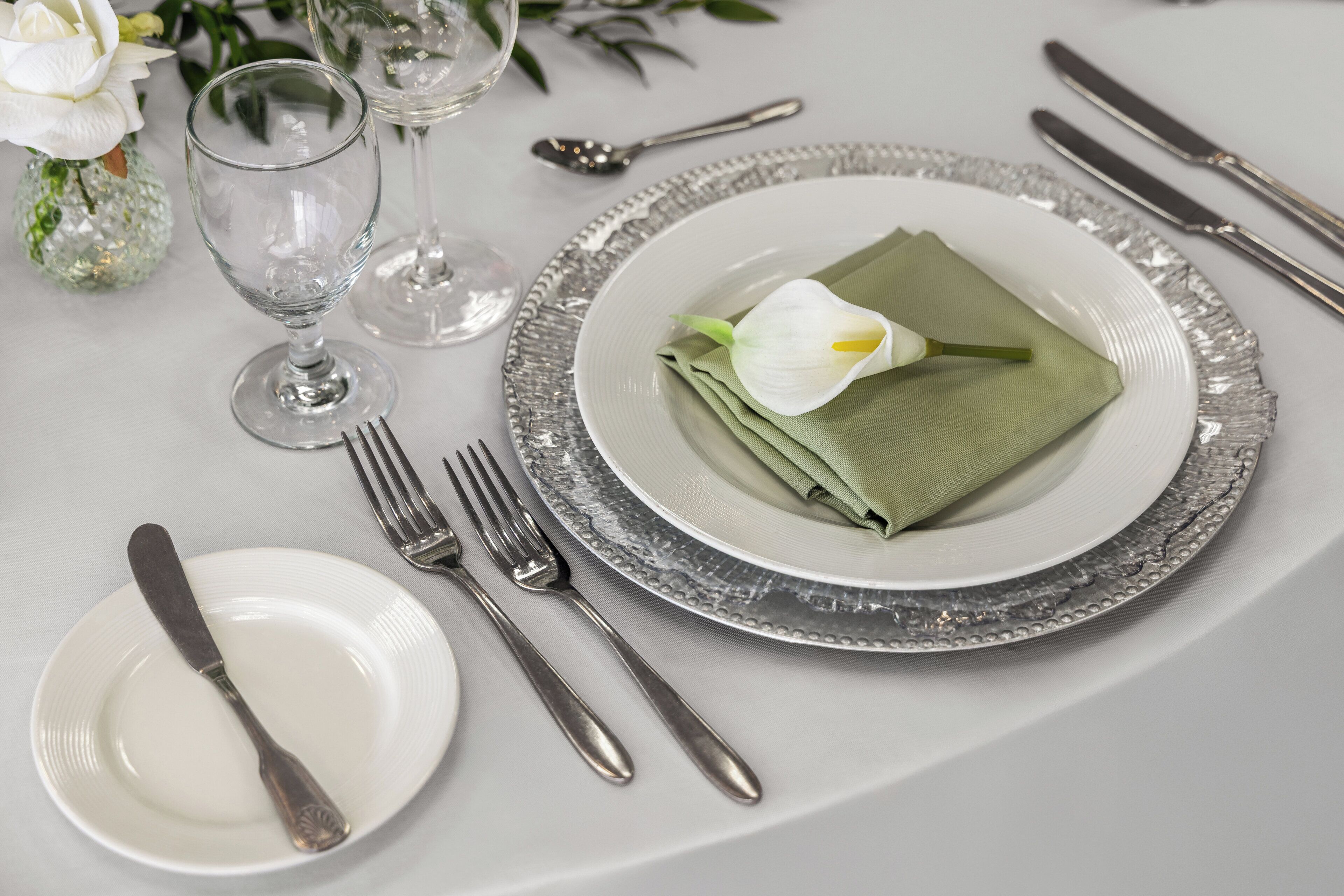Une table dressée avec une assiette blanche, des couverts en argent, un verre et une serviette verte.
