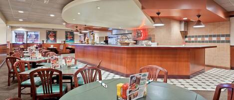 A restaurant with wooden tables and chairs, a central counter, and a tiled floor.